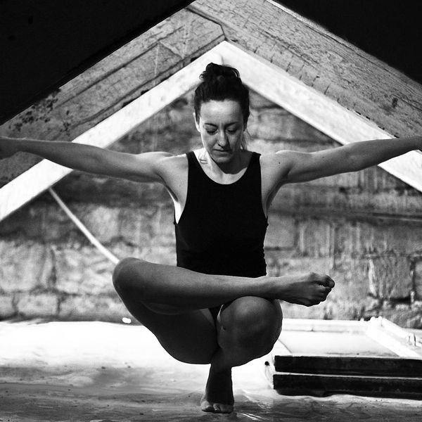 Woman in a graceful yoga pose against a dark background with lavender light.
